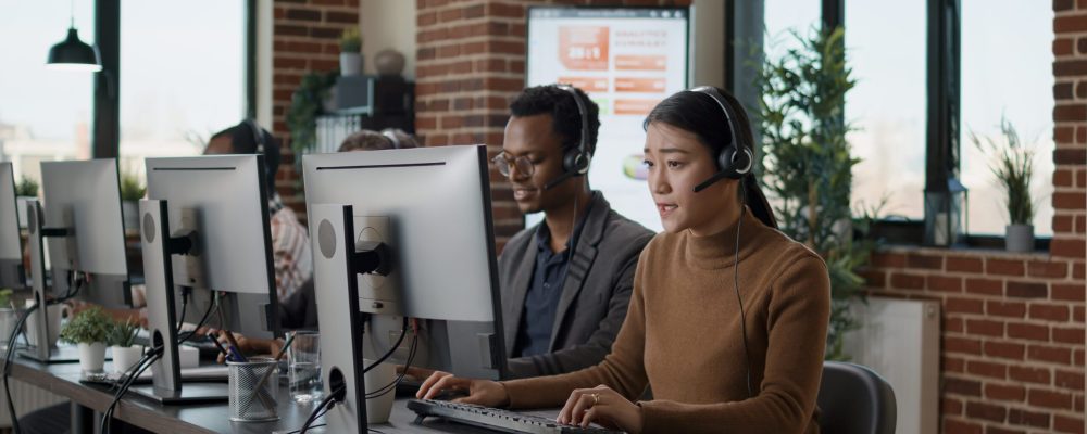 Multiethnic team of people working at call center office, using audio headset for telecommunications to help clients. People answering call on phone helpline, giving assistance at workstation.